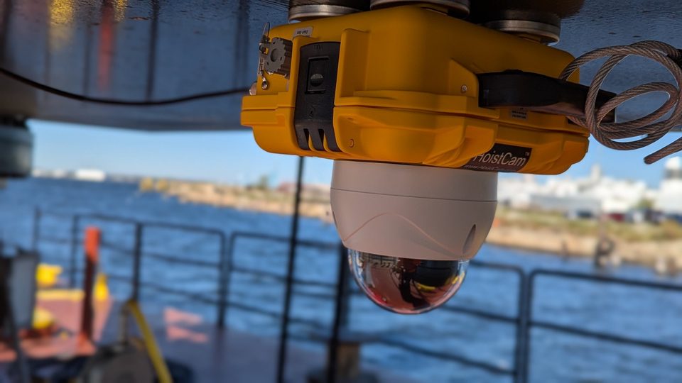 HoistCam HD197 camera mounted under a barge crane boom, looking down at the deck with open water beyond the rail